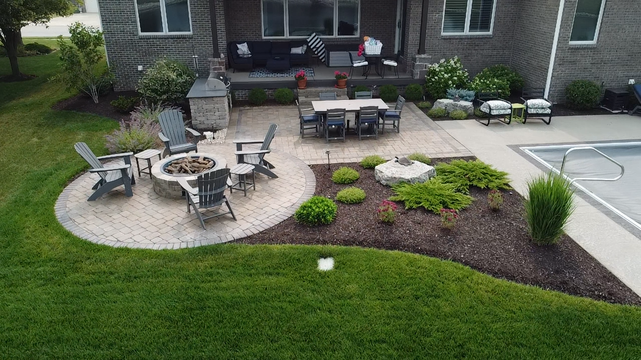 An aerial view of a modern backyard patio with a circular fire pit and seating area